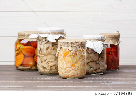 Pickled fermented sauerkraut, tomatoes, peppers, carrots, mushrooms suillaceae, assorted in glass jars on a brown wooden table and white background. 67194393