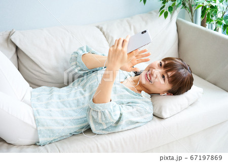 ソファーで寝転ぶ女性 スマホ リラックス ソファーで寝転ぶ女性 スマホ リラックス 67197869