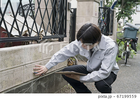 老朽化した住宅の塀を調査するビジネスマン 67199559