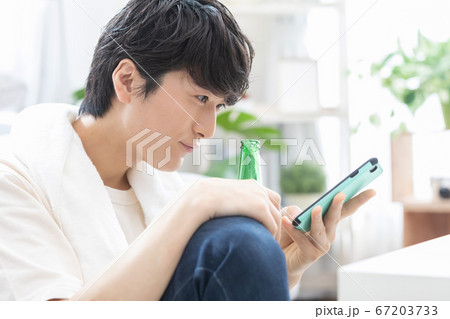 お風呂上りにビールを飲みながらスマホを見る若い男性 67203733