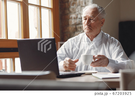 Old man sitting at the table and working with a laptop 67203925