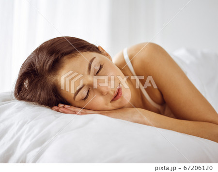 Beautiful young brunette woman sleeping while lying in bed comfortably and blissfully. Good morning concept Beautiful young brunette woman sleeping while lying in bed comfortably and blissfully. Good morning concept 67206120