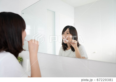 Young asian woman brushing her teeth in front of the bathroom mirror. Dental health care concept. Young asian woman brushing her teeth in front of the bathroom mirror. Dental health care concept. 67220381