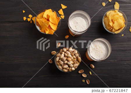 Nachos, chips, pistachios in glass bowls and scattered on wooden table, near are beer with foam in glasses Nachos, chips, pistachios in glass bowls and scattered on wooden table, near are beer with foam in glasses 67221847
