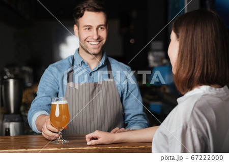 Beer for regular client. Smiling bartender gives to girl lager behind bar Beer for regular client. Smiling bartender gives to girl lager behind bar 67222000