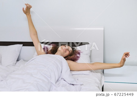 Teen girl waking up in the morning lying on pillow in bed with arms open Teen girl waking up in the morning lying on pillow in bed with arms open 67225449