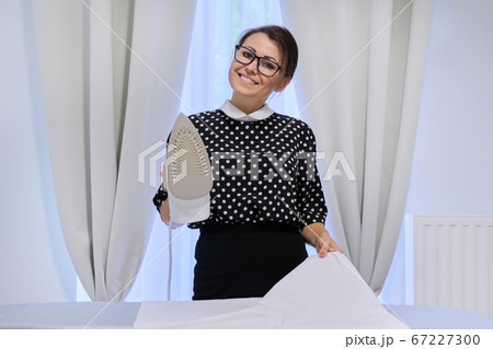 Mature smiling woman with an iron and ironing board Mature smiling woman with an iron and ironing board 67227300