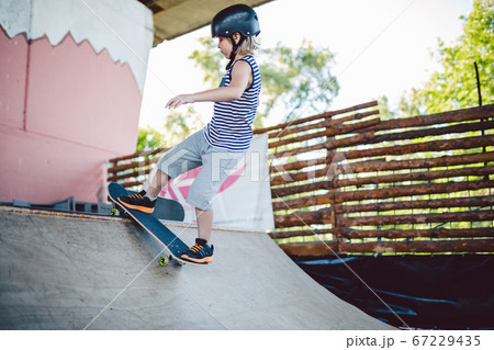 Child skateboarder during learning tricks on a ramp in an urban skate park. boy in a sports helmet rides on a skate board at a sports venue. Active extreme kids spending time. guy skateboarder rides 67229435
