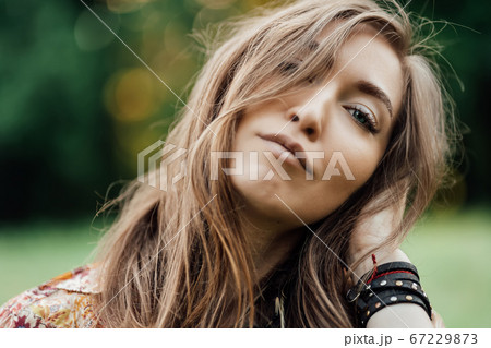 Close up Beautiful young woman wearing bohostyle clothes posing in the rays of the evening sun, sunset. Boho style fashion, female wearing silver jewelry having fun in park outdoors. 67229873