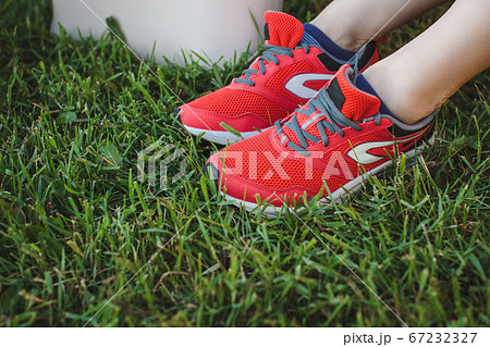 Girl in red sports sneakers sits resting on the grass in the park after jogging. Legs close up. 67232327