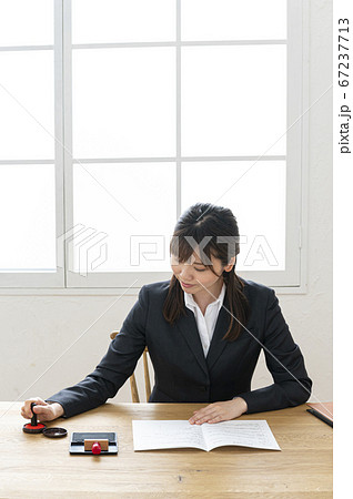ビジネススーツで机で書類に捺印する女性 ビジネススーツで机で書類に捺印する女性 67237713