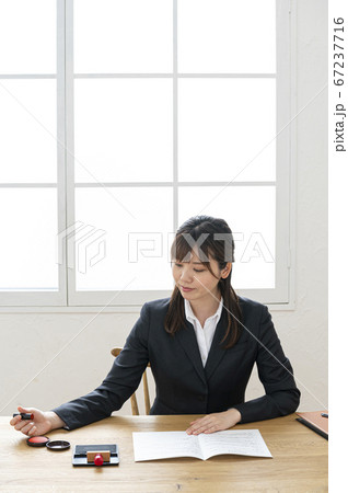 ビジネススーツで机で書類に捺印する女性 67237716