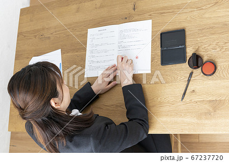 ビジネススーツで机で書類に捺印する女性 67237720