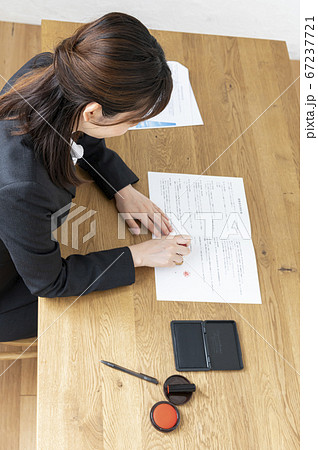 ビジネススーツで机で書類に捺印する女性 67237721