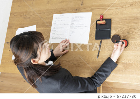 ビジネススーツで机で書類に捺印する女性 67237730