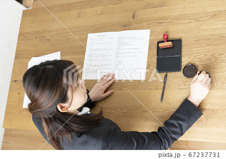 ビジネススーツで机で書類に捺印する女性 67237731
