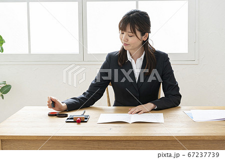 ビジネススーツで机で書類に捺印する女性 ビジネススーツで机で書類に捺印する女性 67237739
