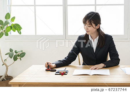 ビジネススーツで机で書類に捺印する女性 ビジネススーツで机で書類に捺印する女性 67237744