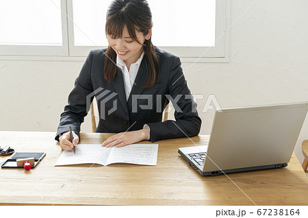 ビジネススーツで机で書類に捺印する女性 67238164