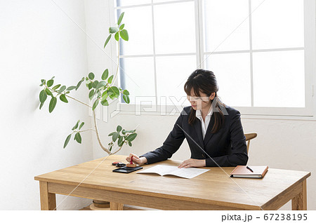ビジネススーツで机で書類に捺印する女性 67238195