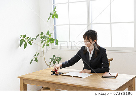 ビジネススーツで机で書類に捺印する女性 67238196