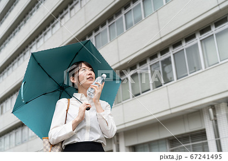 ペットボトルを顔にあてて日傘をさすビジネスウーマン 67241495
