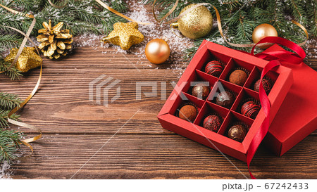 Chocolate candies in a red craft box wooden Christmas background fir branches of a New Year's toy. Flat layout top view. 67242433