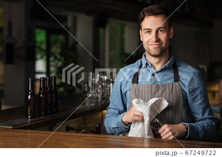 Service at pub. Barman wipes empty glass, standing at bar in interior Service at pub. Barman wipes empty glass, standing at bar in interior 67249722