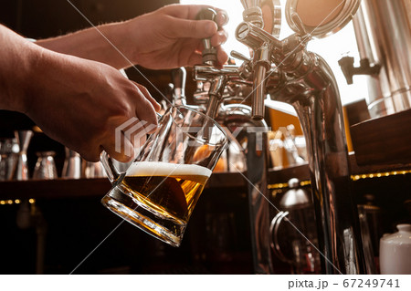 Work bartender. Bartender pours beer from tap in glass mug in interior of pub Work bartender. Bartender pours beer from tap in glass mug in interior of pub 67249741