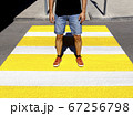 A young man in a black T-shirt and denim shorts stands at a pedestrian crossing 67256798
