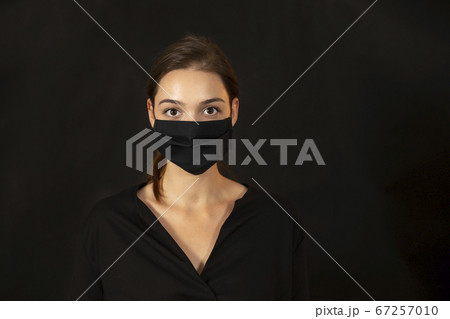 Studio portrait of a young woman wearing a face mask on dark background. Studio portrait of a young woman wearing a face mask on dark background. 67257010