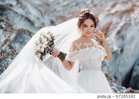Beautiful bride in a wedding dress with a bouquet on the top of the salt mountains. A stunning young bride with curly hair . Wedding day. . Beautiful portrait of the bride without the groom. 67265392