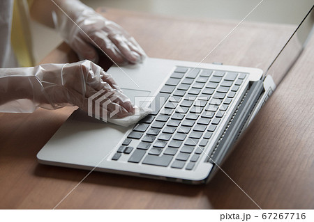 ノートパソコンを除菌シートで拭くビニール手袋をつけた女性の手元の写真素材