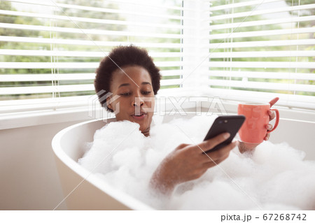 Woman with coffee cup using smartphone in a bathtub 67268742