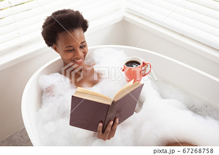 Woman with coffee cup reading book in a bathtub 67268758