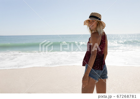 Woman wearing hat smiling while standing on the beach Woman wearing hat smiling while standing on the beach 67268781