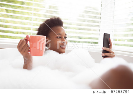 Woman with coffee cup using smartphone in a bathtub Woman with coffee cup using smartphone in a bathtub 67268794