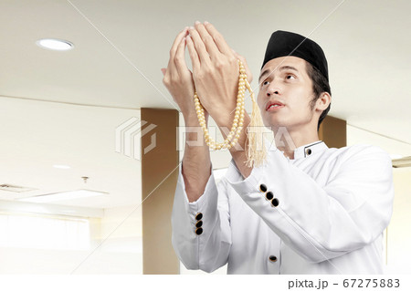 Asian Muslim man praying with prayer beads on his Asian Muslim man praying with prayer beads on his 67275883
