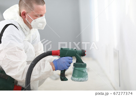 Man in mask holds spray gun in his hands and paints the wall 67277374