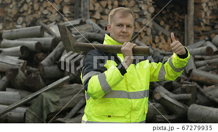 Lumberjack in reflective jacket. Man woodcutter with big axe. Sawn logs, firewood background 67279935