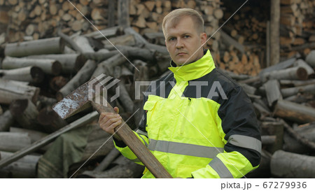 Lumberjack in reflective jacket. Man woodcutter with huge axe. Sawn logs, firewood background 67279936