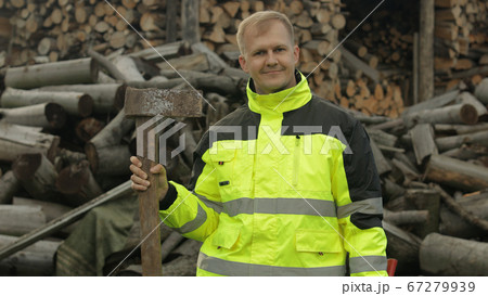Lumberjack in reflective jacket. Man woodcutter with huge axe. Sawn logs, firewood background Lumberjack in reflective jacket. Man woodcutter with huge axe. Sawn logs, firewood background 67279939