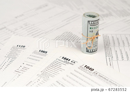 Tax forms lies near roll of hundred dollar bills. Tax forms lies near roll of hundred dollar bills. 67283552