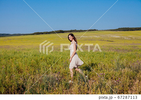 Beautiful woman in dress walks on the field with yellow flowers Beautiful woman in dress walks on the field with yellow flowers 67287113