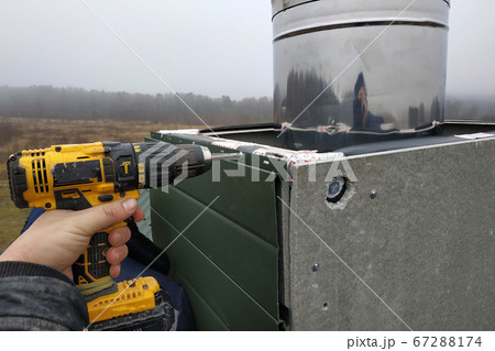 A worker on the roof of the house sheathes the chimney with a metal profile 67288174
