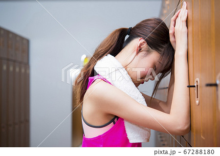 スポーツジムのロッカーで悩む若い女性 67288180