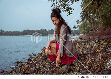 Girl with dreadlocks sits on a rocky beach Girl with dreadlocks sits on a rocky beach 67308418