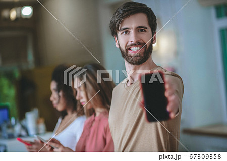 Smiling man holding smartphone in outstretched arm, two girls behind 67309358