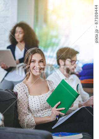 Girl with book looking at camera, friends at distance busy 67309444