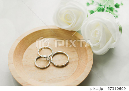 白いバラが添えられた木目小皿の上の婚約指輪と結婚指輪の写真素材